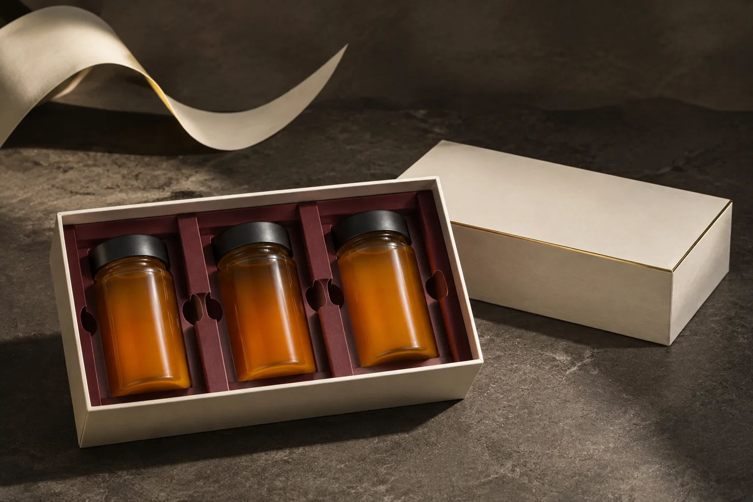 Illustrative ivory gourmet gift box with three honey jars separated by a burgundy insert