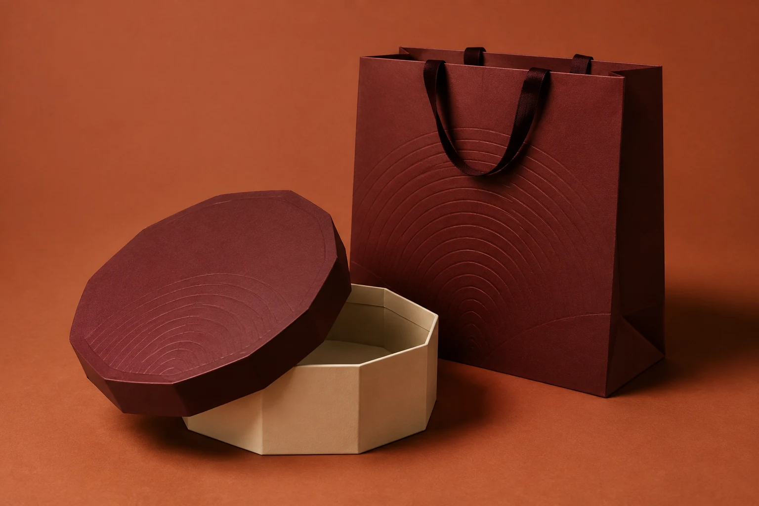 Illustrative ivory and burgundy octagonal presentation box with a matching shopping bag and embossed arc motif